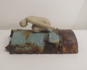 a small ceramic figure on a piece of pipe
